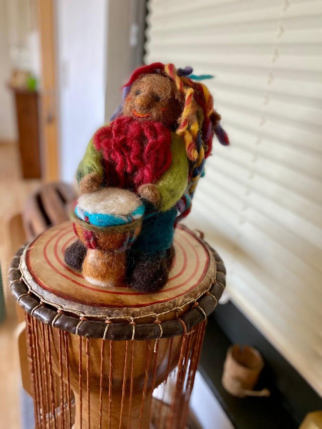 Eine Djembe auf der eine Filzfigur (ein Rastamann mit Djembe) platziert ist.