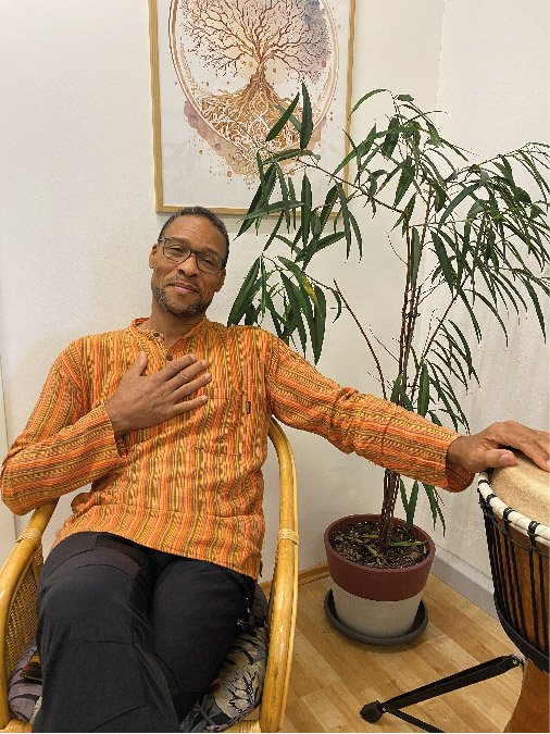 Jean-Marc Dégras in einem Sessel legt eine Hand auf das Herz die andere Hand liegt auf einer Djemne