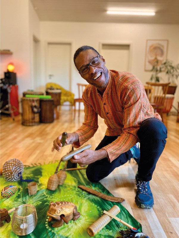 Jean-Marc Dégras kniet neben einer Sammlung von Percussion-Instrumenten und lächelt in die Kamera